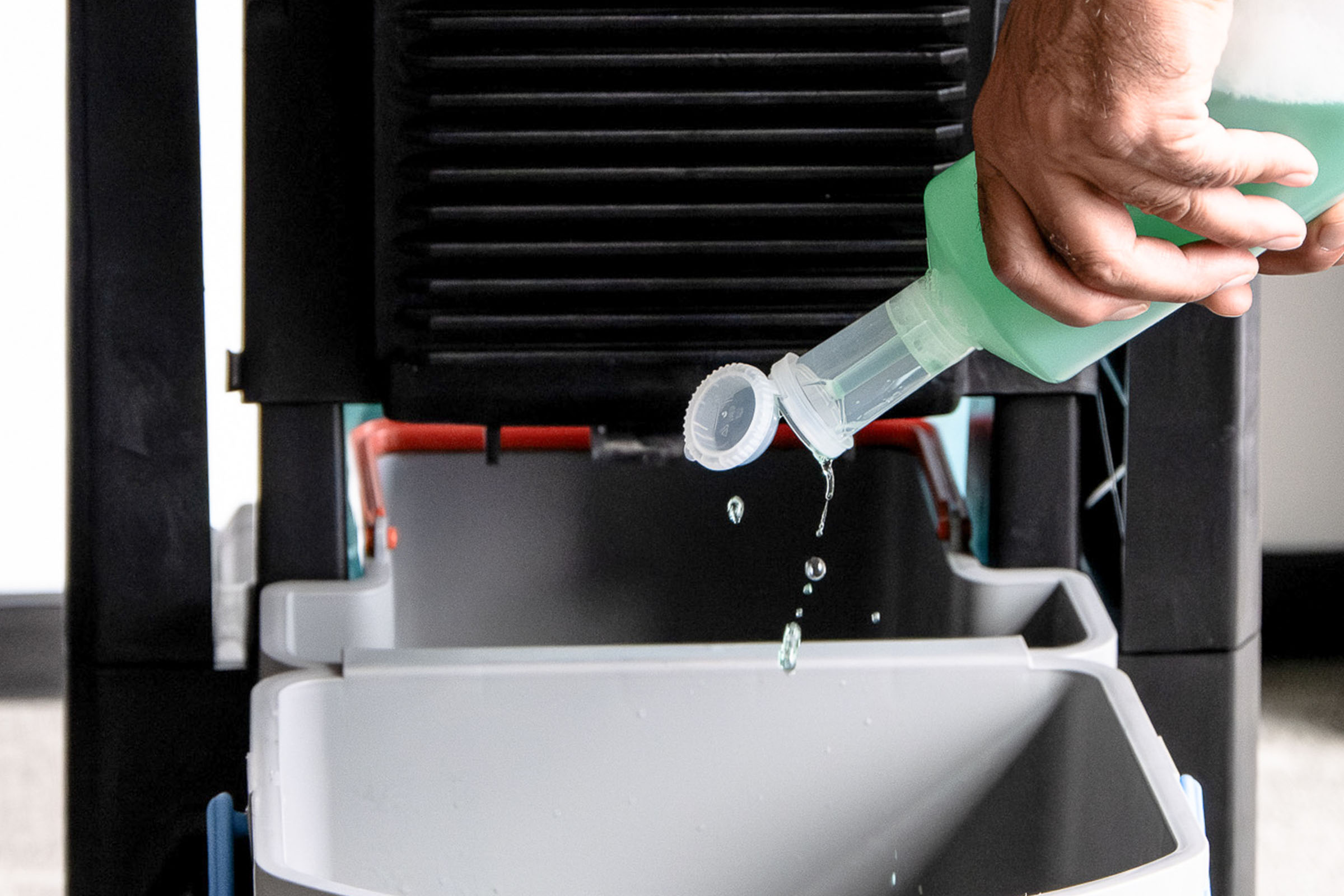 Hand dosiert grünes Reinigungsmittel in einen Reinigungseimer